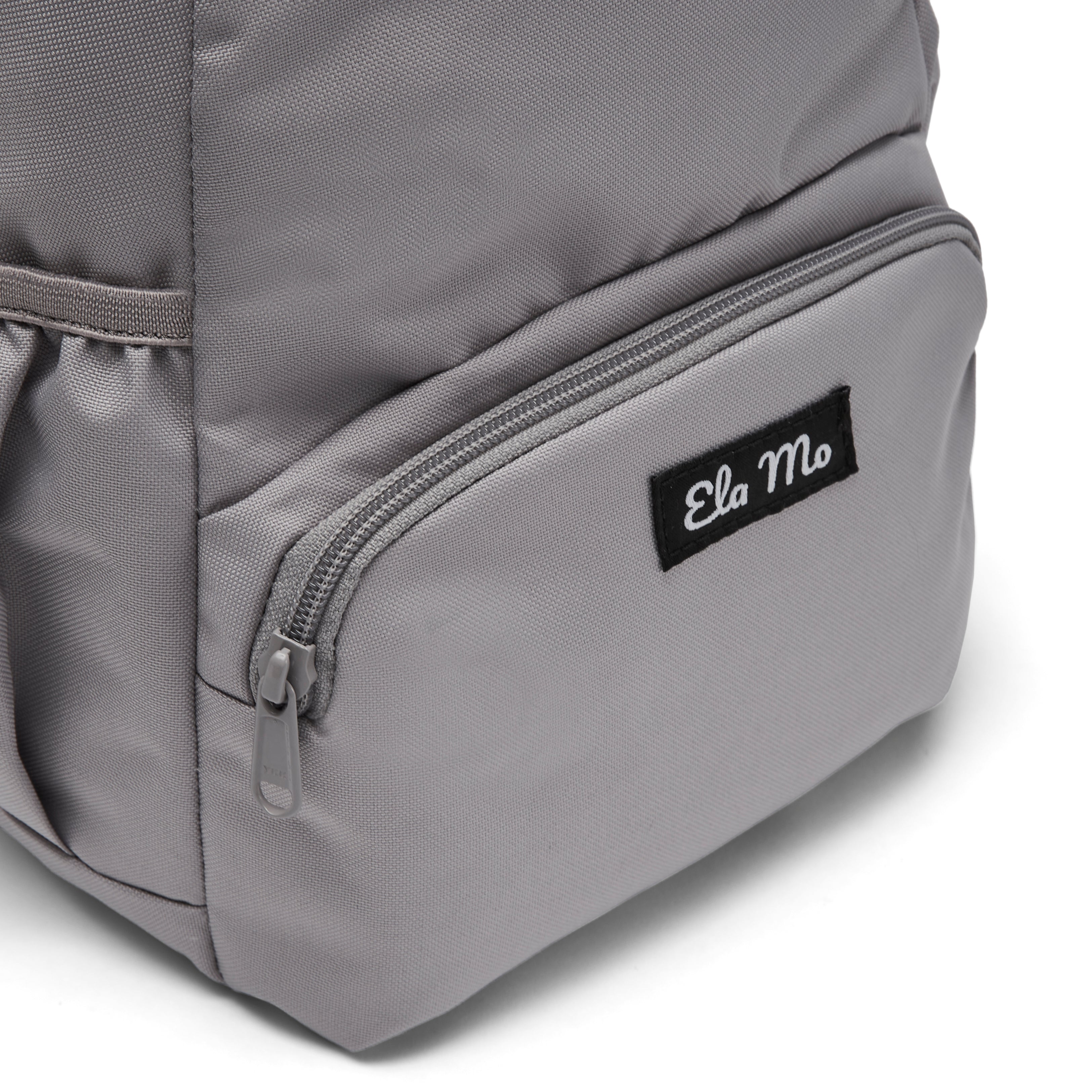 Ela Mo™ Mini Rucksack | Warm Grey. Außenfach mit Herstellerlogo auf der Vorderseite des Rucksacks.