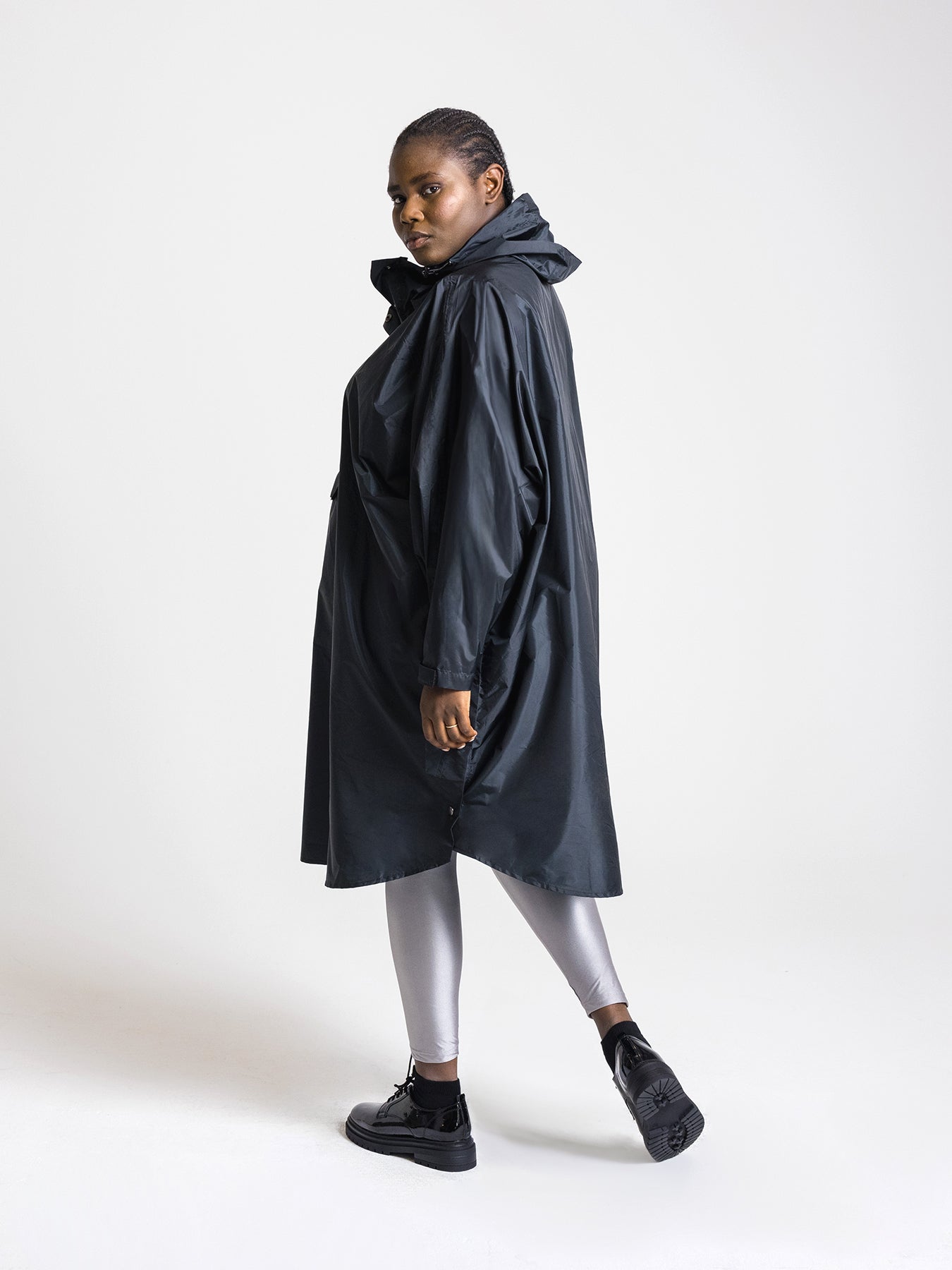Ela Mo™ Regenponcho | Black. Frau mit Regenponcho von der linken Seite auf weißem Hintergrund.
