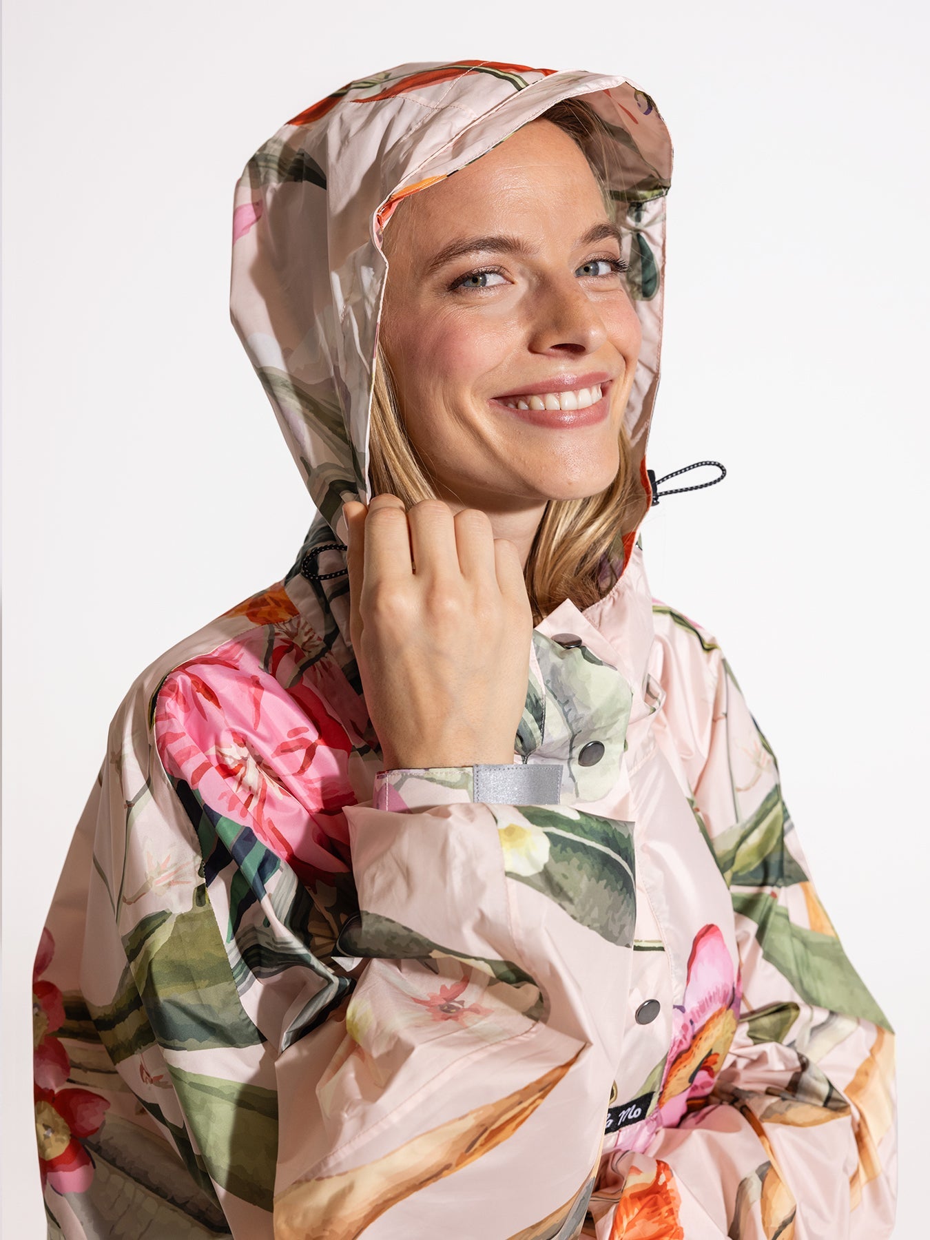 Ela Mo™ Regenponcho | Luxe. Eine Frau im Regenponcho mit hohem Kragen und Kaputze.