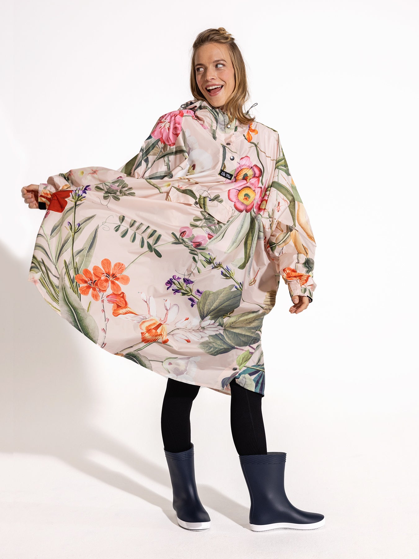 Ela Mo™ Regenponcho | Luxe. Eine Frau im Regenponcho, der ausreichend breit ist, auf weißem Hintergrund.