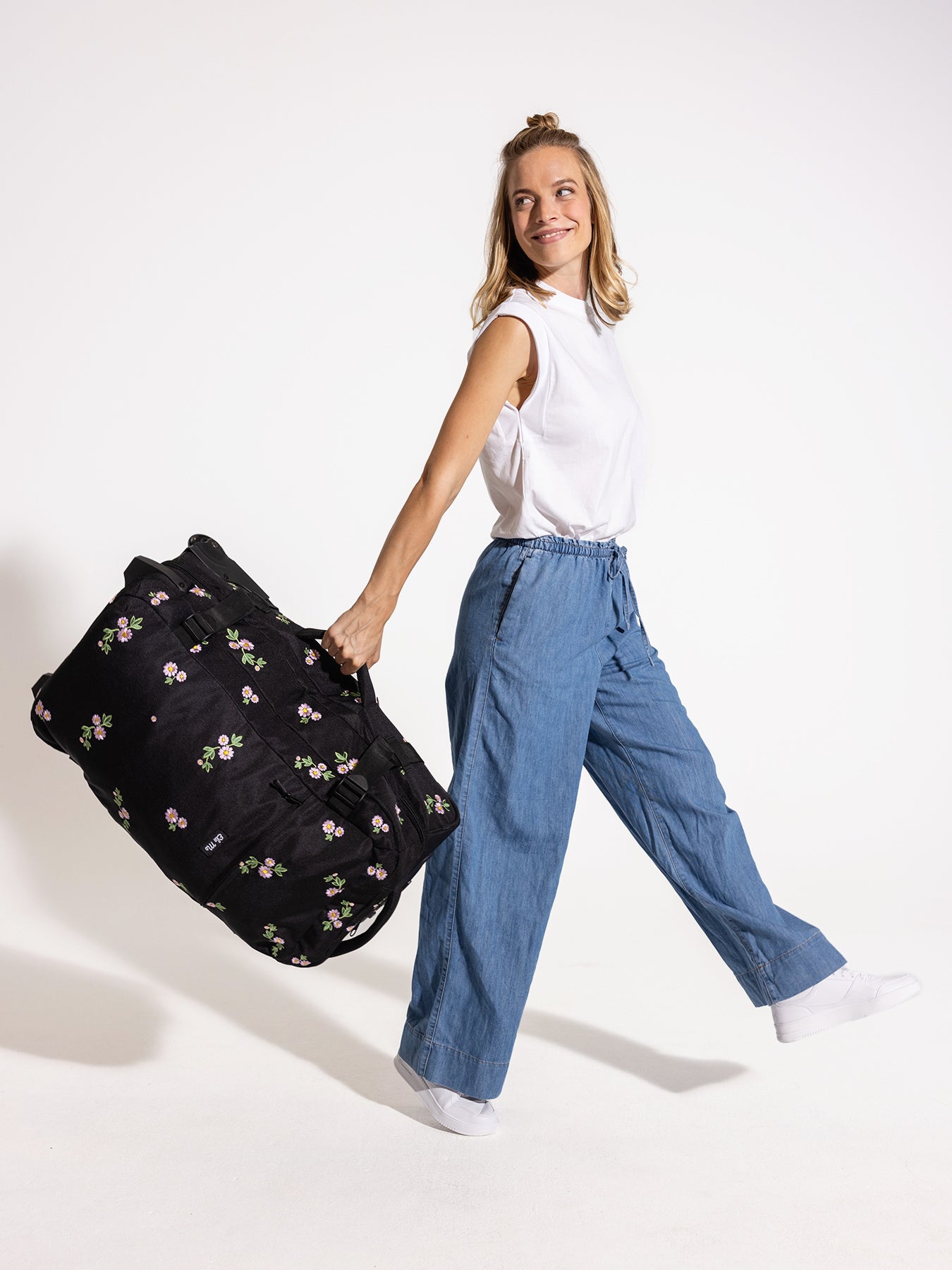 Ela Mo™ Reisetasche mit Rollen 78 Liter | Embroidery Edition Upsy Daisy. Frau mit der Tasche am Seitengriff in der Hand.